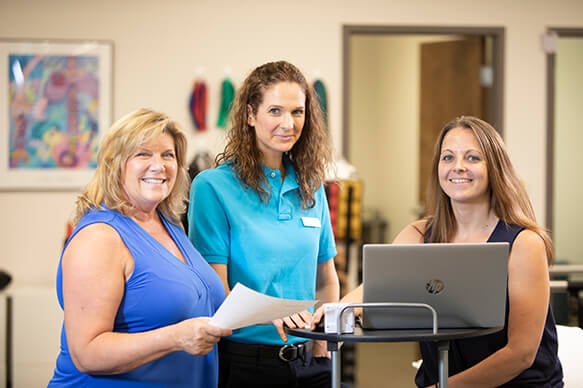 Three female therapists standing next to a rolling desk and using a laptop