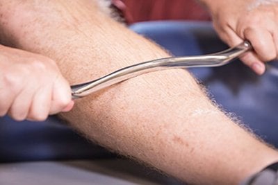 Hands pulling a curved metal rod with handles up a man's calf.