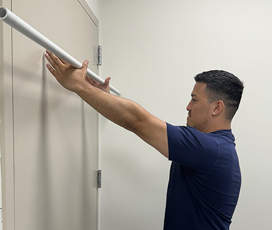 A male physical therapist raising a pole upward with his shoulder muscles. 