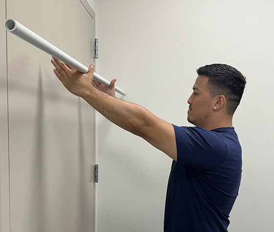 A male physical therapist lifting a pole to the wall in front of him.  