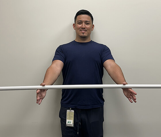 A male physical therapist holding a pole between his two thumbs and stretching out his arms. 