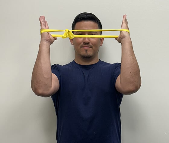 A male physical therapist with an exercise band wrapped around his hands, stretching them outward. 