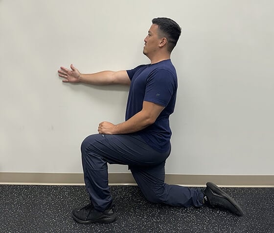 A male physical therapist in windmill position one, with his right arm flat against a wall. 