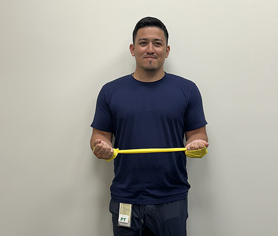 A male physical therapist stretching an exercise band outward. 