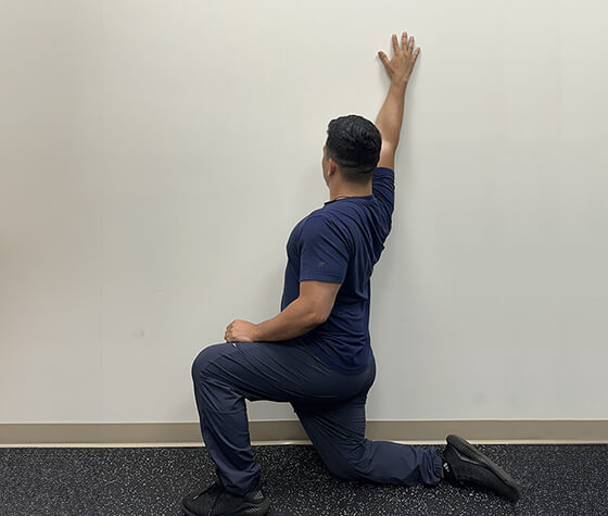 A male physical therapist in windmill position three, with his arm fully raised in front of his head. 