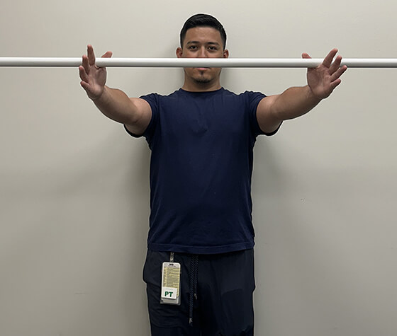 A male physical therapist raising a pole with his shoulder muscles. 