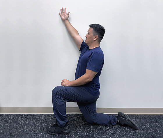 A male physical therapist in windmill position two, with his arm slightly raised in front of his head. 