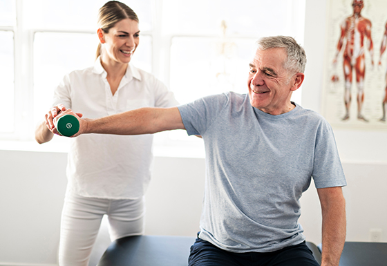 A female physical therapist helping a patient lift a dumbbell to stretch his elbow. 